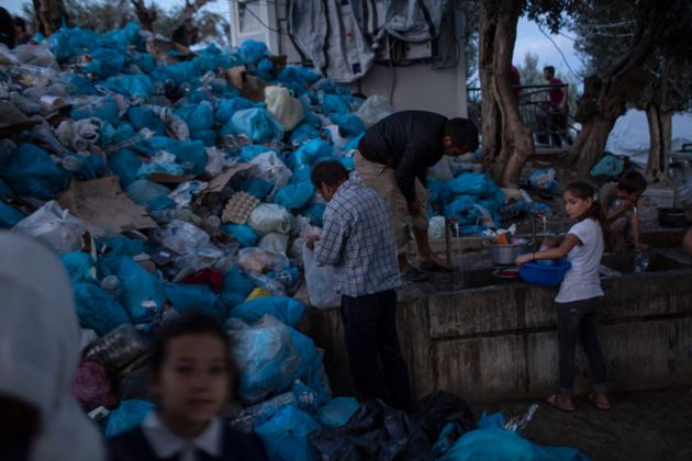 Ανθρωποι πλένονται μπροστά από ένα σωρό σκουπιδιών, σε ένα αυτοσχέδιο καταυλισμό δίπλα στο υπερπλήρες κέντρο της Μόριας.