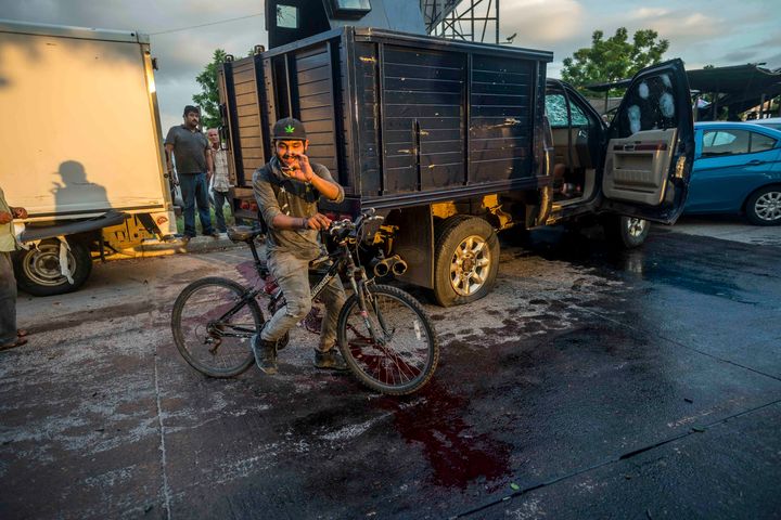 A man handles a bullet cartridge in a blooded street by a truck with a flat tire and covered with bullet hits after a gunfight in Culiacan, Mexico, Thursday, October 17.