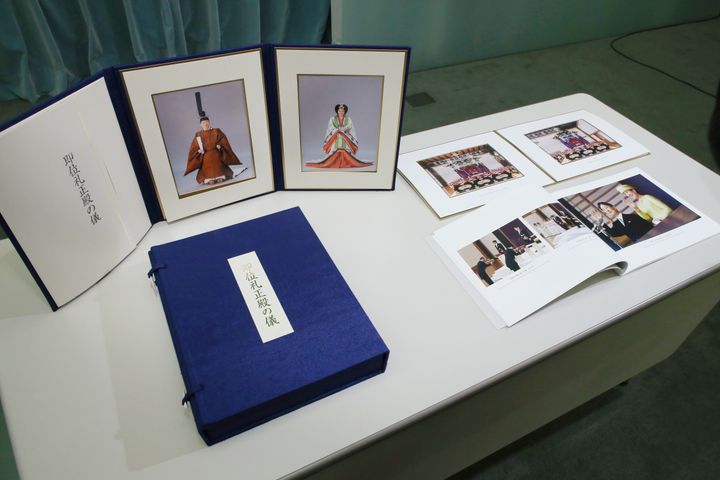 「即位礼正殿の儀」で参列者に配られる記念品。装束姿の天皇、皇后両陛下の写真と式次第。「高御座と御帳台」（右上）、「皇室と皇居」という題が付いたアルバム（同下）。三つセットで手前の青い箱に収められている＝１８日、首相官邸