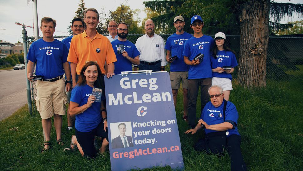 Conservative candidate Greg McLean, in orange shirt, with his wife Ruth, kneeling on the left, pose for a photo with campaign volunteers in July 2019.