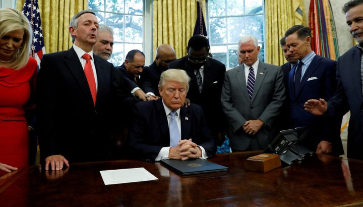 Faith leaders place their hands on the shoulders of President Donald Trump as he takes part in a prayer for those affected by Hurricane Harvey in the Oval Office on Sept. 1, 2017.