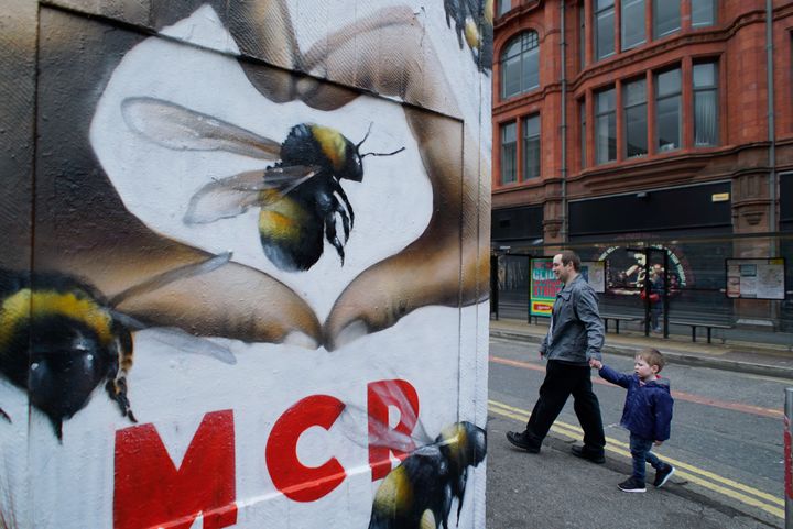 People walk past a graffiti on a wall depicting bees in Manchester, Sunday, May 28, 2017. 