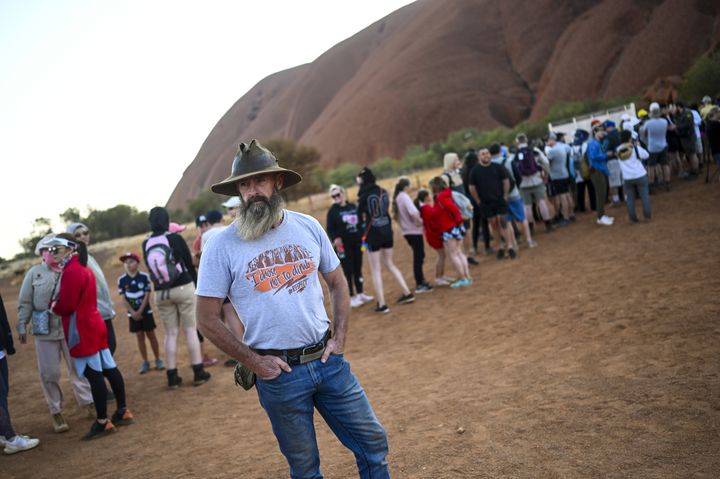 A man wearing a T-shirt saying "I chose not to climb" stands next to tourists lining up to climb Uluru, formerly known as Ayers Rock, at Uluru-Kata Tjuta National Park in the Northern Territory.