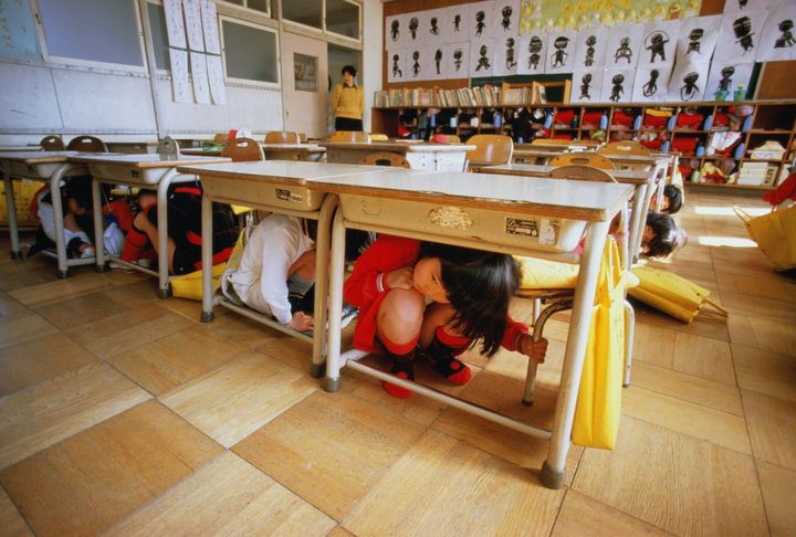 In this image, children in Japan experience in an earthquake drill at school. Today, students in countries all around the world are required to participate in many different kinds of "preparedness" drills but the author argues, "emergency simulations are for EMTs, SWAT teams and teachers — not for 6- and 7-year-olds who should focus on being kind, standing up to bullies and playing four square at recess."