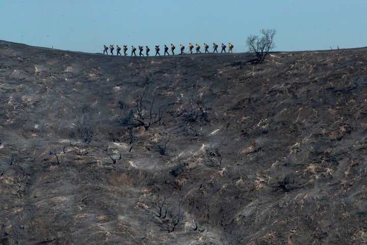 Fire crews walk along a blackened ridge as they battle the Getty fire Monday in Los Angeles.