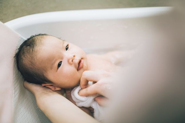 Mother bathing smiling new born baby in bathtub