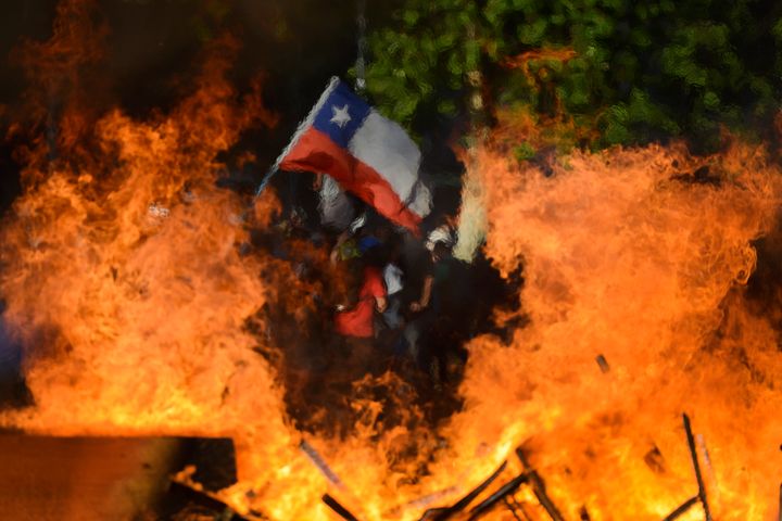 Seen through a burning street barricade, an anti-government demonstrator waves a Chilean flag in Santiago, Chile, on Oct. 28,