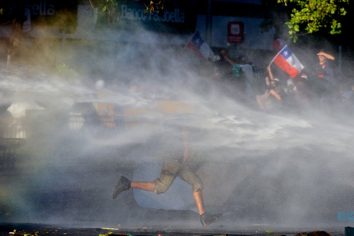 An anti-government protester runs through spray coming from a police water cannon in Santiago, Chile, on Oct. 28, 2019.&nbsp;