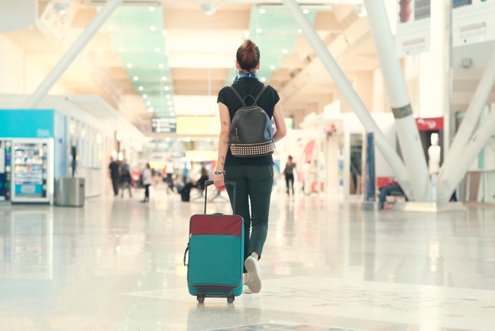 Back view of woman pulling her luggage strolling inside the airport terminal