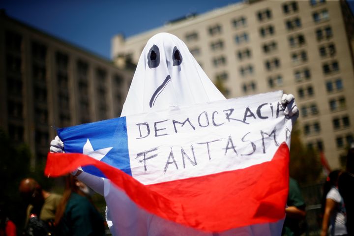 A demonstrator dressed as a ghost holds a Chilean flag with the legend "ghost democracy" during anti-government protests in Santiago, Chile.