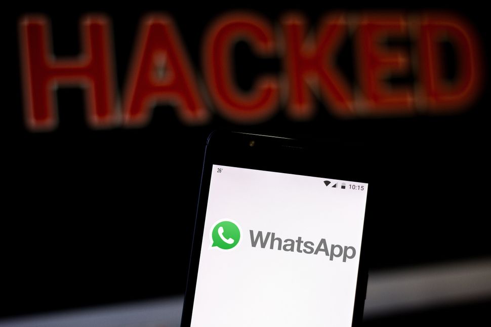 In this photo illustration, the WhatsApp logo is seen displayed on a smartphone and red alerting word HACKED on the blurred background. Conceptual photo for data breach. 