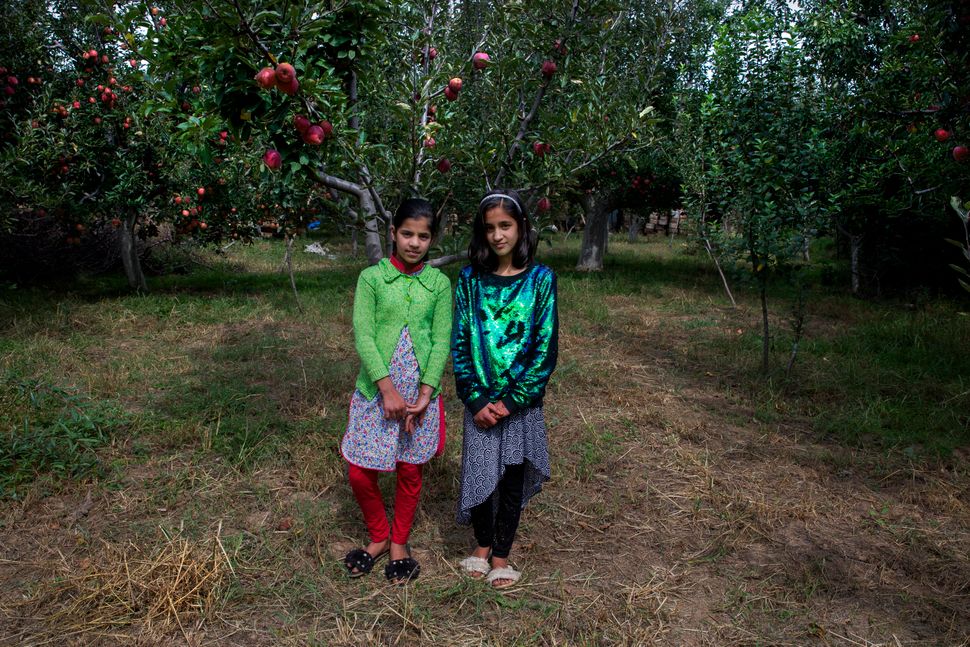 In this Oct. 6, 2019, photo, twin sisters Tabeer Shafi Bhat, right, and Taseer Shafi Bhat stand for photographs inside an apple orchard in Wuyan, south of Srinagar. The girls said that they've had nothing to do since the lockdown started on Aug. 5 and that they miss going to school. Authorities encouraged students to return to school but parents have largely remained unwilling to send their kids to educational institutes due to the restrictions in place. 