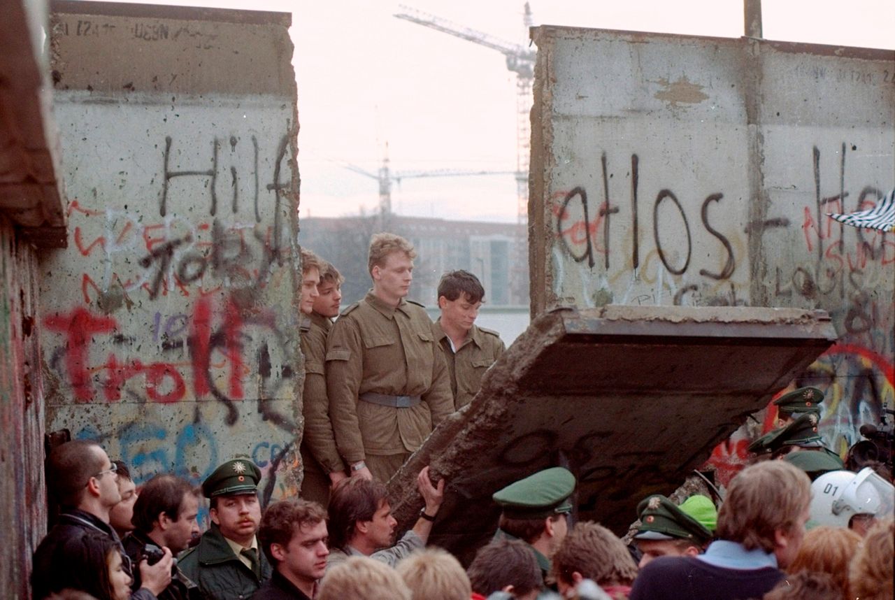 East German border guards are seen through a gap in the Berlin wall after demonstrators pulled down a segment of the wall at Brandenburg gate, Berlin, 11 November 1989.