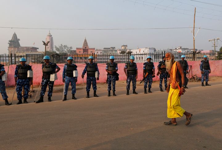A sadhu walks past security officers standing guard in Ayodhya, Saturday, Nov. 9, 2019. 