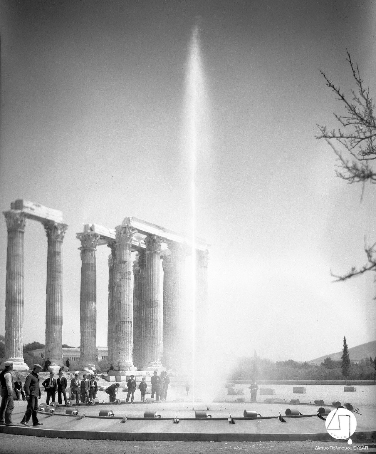 Στιγμιότυπο από την τελετή εγκαινίων του νέου δικτύου ύδρευσης των πόλεων Αθηνών, Πειραιώς και περιχώρων, στους Στύλους του Ολυμπίου Διός, 03 Ιουνίου 1931. Η Ελληνική Εταιρεία Υδάτων διαφημίζεται μέσω της τοποθέτησης πιδάκων νερού στην τελετή των εγκαινίων.