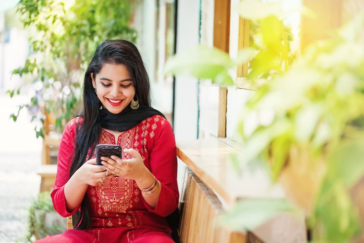 Pretty young indian woman using her phone and looking at camera