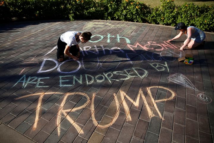 Darby Dunlop, left and Zoe Stein of NextGen America write a message that both Republican U.S. Senate candidate Rep. Martha McSally and Arizona Governor Doug Ducey are endorsed by Donald Trump next to a line of people waiting to vote at the ASU Palo Verde West polling station during the U.S. midterm elections in Tempe, Arizona, Nov, 6, 2018.