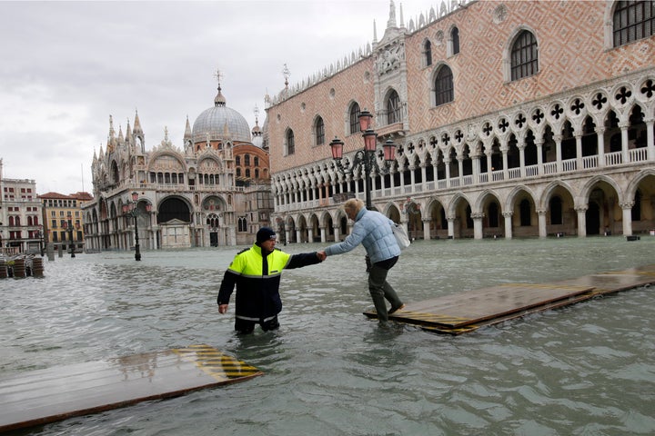 A city worker helps a woman who decided to cross St. Mark's Square on a gangway, in spite of it being closed, in Venice, Ital
