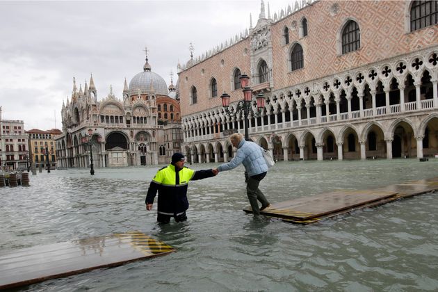 A city worker helps a woman who decided to cross St Mark's Square on a gangway, in spite of it being closed, in Venice, Italy, on Sunday.