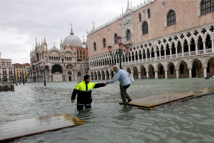 A city worker helps a woman who decided to cross St. Mark's Square on a gangway, in spite of it being closed, in Venice, Italy, on Nov. 17, 2019. 
