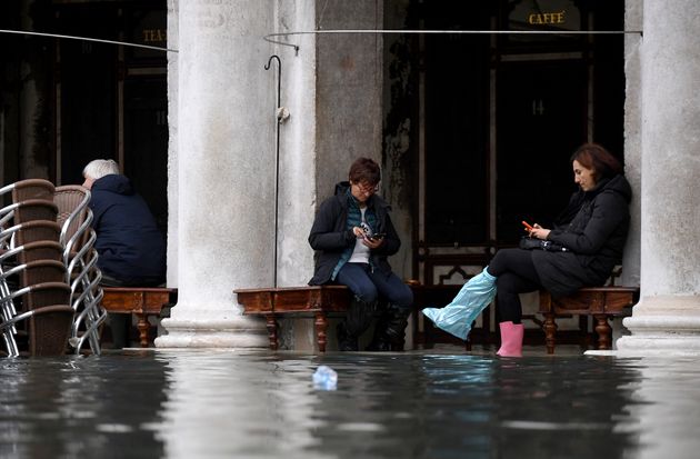 People sit outside a cafe under arcades at St Mark's Square during high tide in Venice, Italy, on Sunday.