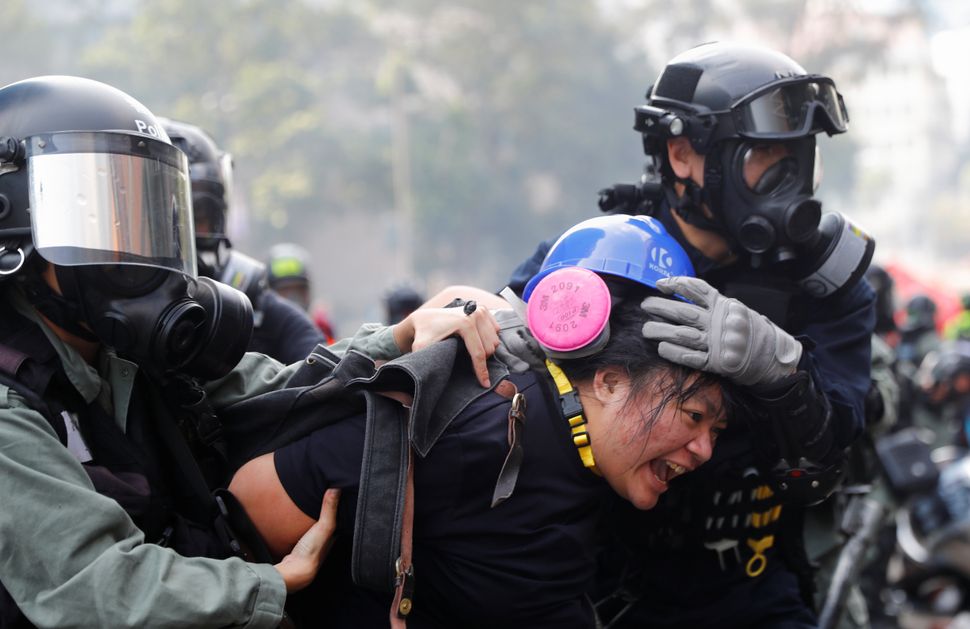 A protester is detained by riot police while attempting to leave campus