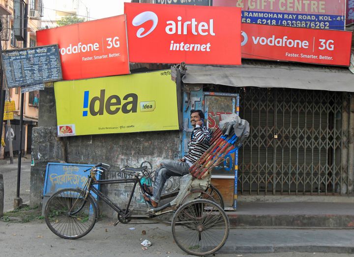 A rickshaw puller speaks on his mobile phone as he waits for customers in front of advertisement billboards belonging to telecom companies in Kolkata.