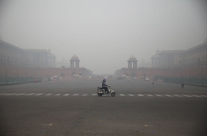 A man rides a scooter wearing a face-mask as Rashtrapati Bhavan in the backdrop is seen engulfed with dense smog in the early morning in New Delhi. 