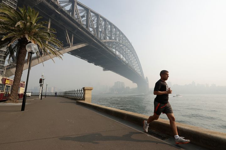Ενας άνδρας τρέχει κάτω από τη γέφυρα στο λιμάνι του Σίδνεϊ, ενώ πυκνός καπνός σκεπάζει την πόλη. Η ετήσια περίοδος των πυρκαγιών της Αυστραλίας άρχισε πολύ νωρίς το 2019, έπειτα από ένα ασυνήθιστα ξηρό και ζεστό χειμώνα.