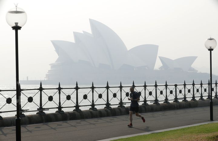 Ενας άνδρας τρέχει κάτω από τη γέφυρα στο λιμάνι του Σίδνεϊ, ενώ πυκνός καπνός σκεπάζει την πόλη. Η ετήσια περίοδος των πυρκαγιών της Αυστραλίας άρχισε πολύ νωρίς το 2019, έπειτα από ένα ασυνήθιστα ξηρό και ζεστό χειμώνα.
