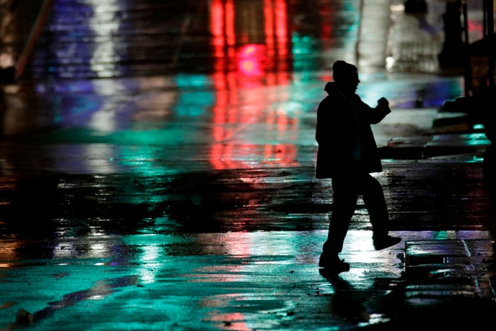 A man is silhouetted as he crosses a rain-covered street on a cold windy night on Nov. 26, 2019, in Kansas City, Mo. The area is forecast to have cold wet weather for the Thanksgiving holiday.