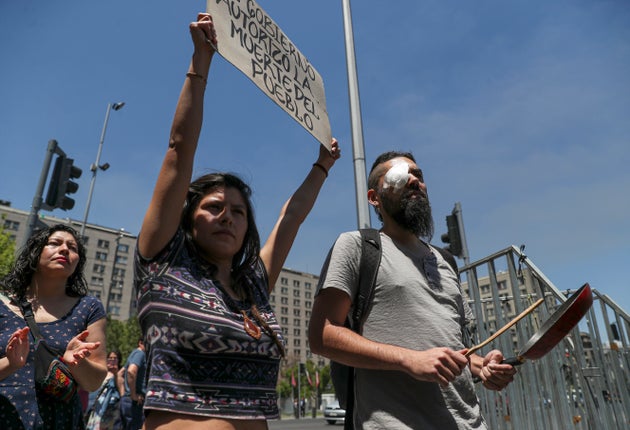 Marcelo Herrera, his eye bandaged from an injury he received during recent protests, bangs on a pan as a woman holds a sign with a message that reads in Spanish: 