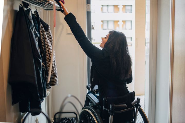 Rear view of young disabled woman reaching for rack on doorway at home