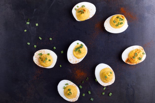 Deviled eggs topped with green onion and paprika over gray background viewed from