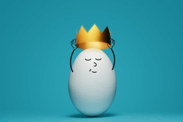 A white egg is dressing a gold crown on blue background. Concept of