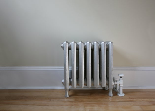a silver hot water radiator against a pale sage coloured wall,