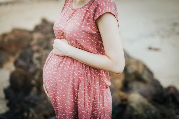 Close up of an expecting pregnant woman wearing a pink dress and holding her belly and relaxing outdoor