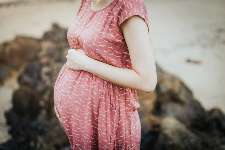 Close up of an expecting pregnant woman wearing a pink dress and holding her belly and relaxing outdoor