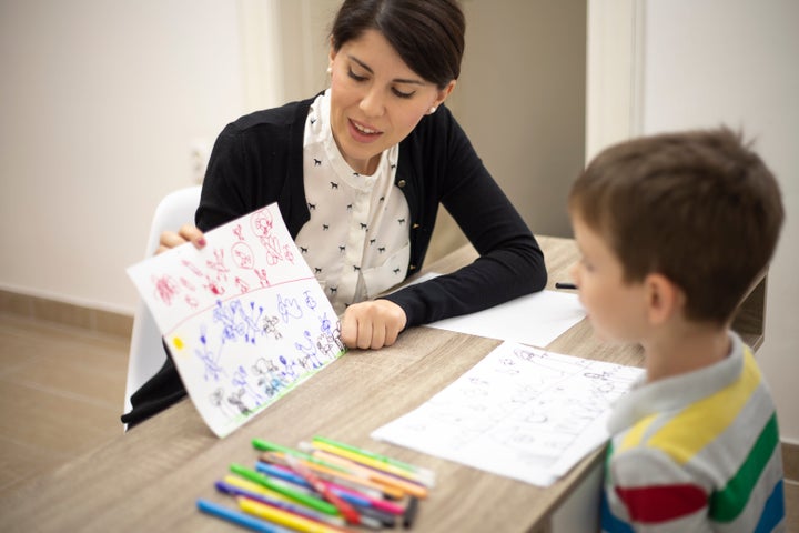A five-year-old boy reviews his drawings with a therapist in this stock image. A new study suggests younger siblings of children with autism should be getting tested before any symptoms appear.