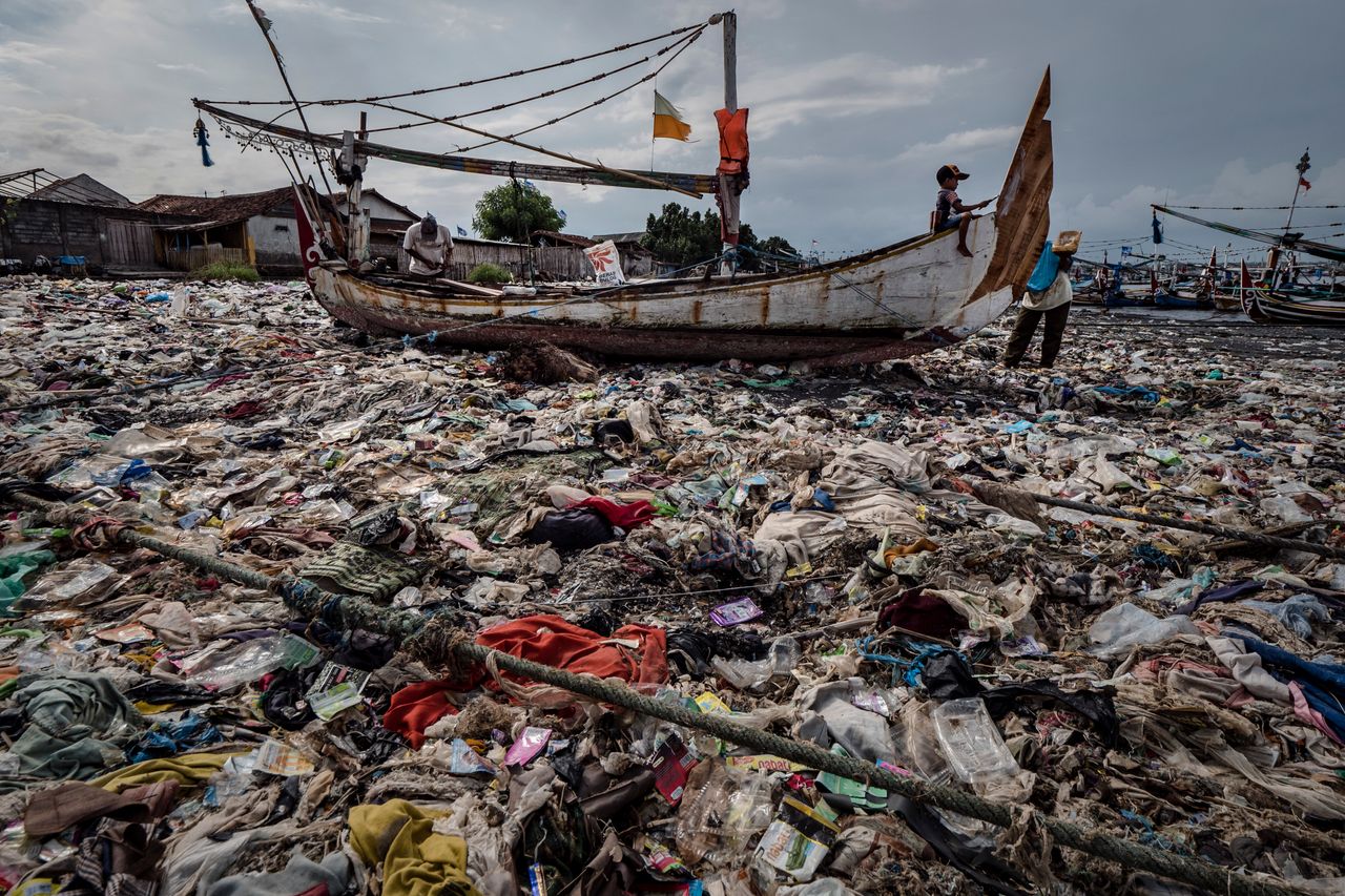 A boy paints a boat in a beach filled with plastic waste at Muncar port in Banyuwangi, East Java on March 4, 2019, in Indonesia.