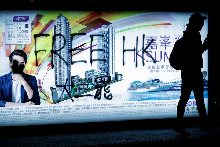 A pro-democracy protester walks by a spray-painted advertisement as demonstrators gather on a street during a protest in Hong Kong, Sunday, Dec. 8, 2019. (AP Photo/Vincent Thian)