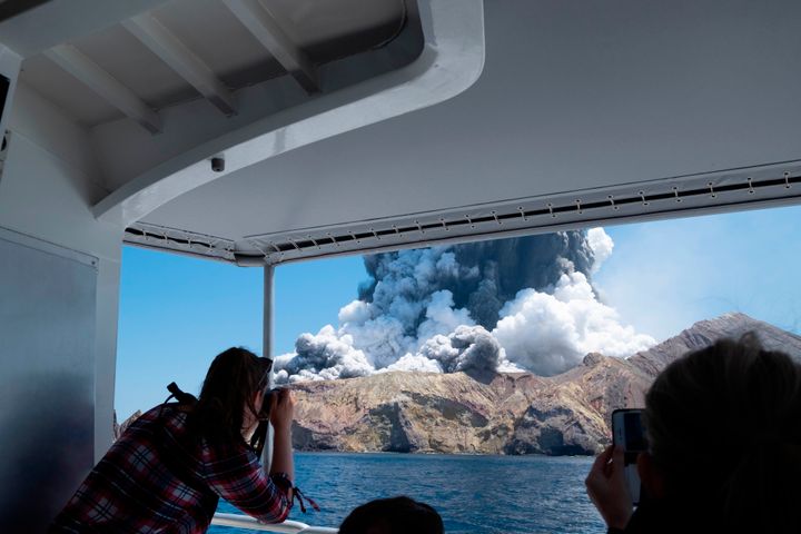 In this Dec. 9, 2019, photo provided by Michael Schade, tourists on a bout film the eruption of the volcano on White Island, New Zealand. Unstable conditions continued to hamper rescue workers from searching for people missing and feared dead after the volcano off the New Zealand coast erupted in a towering blast of ash and scalding steam while dozens of tourists explored its moon-like surface. (Michael Schade via AP)