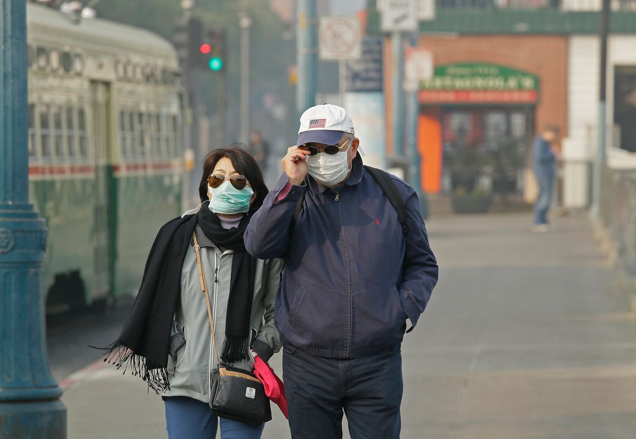 A couple at Fisherman's Wharf in San Francisco wears masks while walking through smoke and haze from wildfires in November 2018.