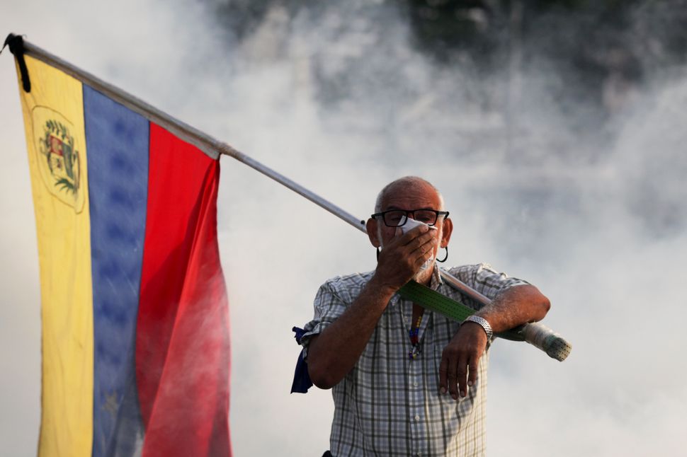 Un oponente de Maduro con una bandera venezolana se cubre la cara contra el gas lacrimógeno disparado durante un intento de levantamiento militar