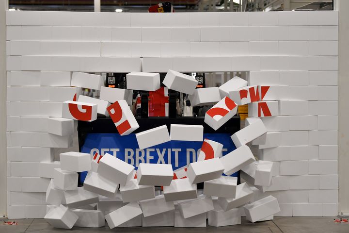 Boris Johnson drives a Union flag-themed JCB, with the words "Get Brexit Done" inside the digger bucket, through a fake wall emblazoned with the word "GRIDLOCK", during a general election campaign event. 
