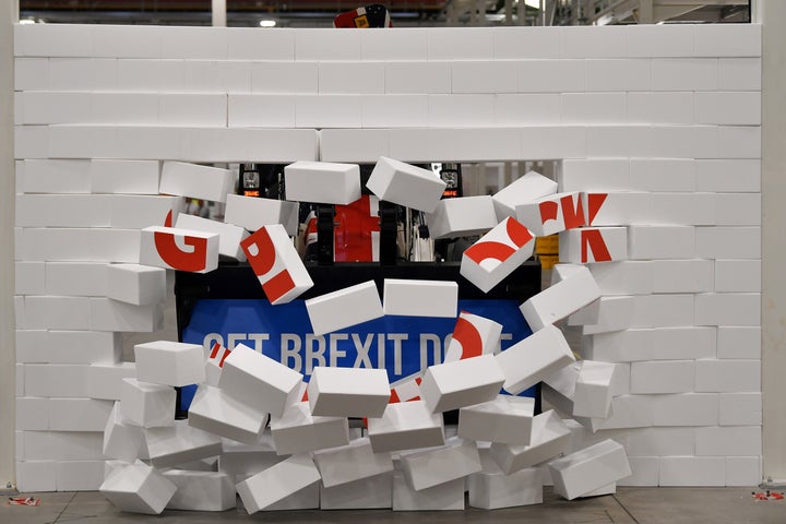 Boris Johnson drives a Union flag-themed JCB, with the words "Get Brexit Done" inside the digger bucket, through a fake wall emblazoned with the word "GRIDLOCK", during a general election campaign event.