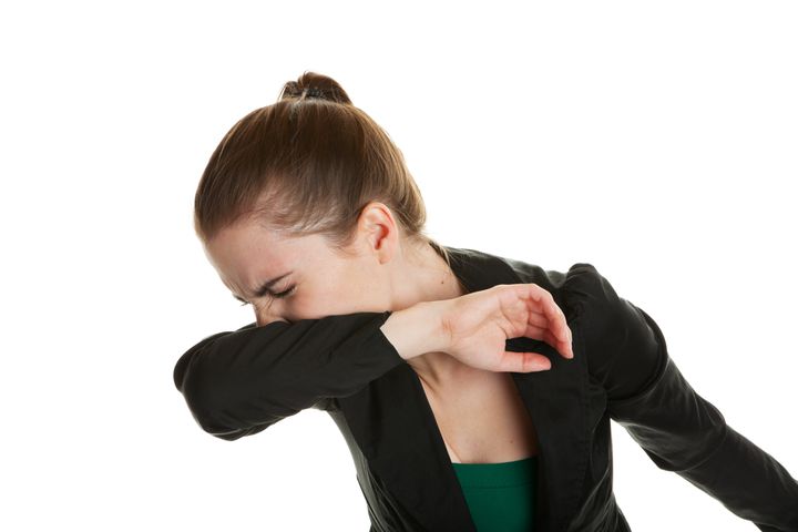 咳のエチケット A young business woman, sneezing into her sleeve to prevent spreading germs. Shot on white background.