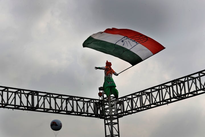 An opposition Congress party worker waves party flag standing atop a steel scaffolding at a rally organized by party to prote