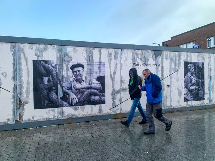 13 Δεκεμβρίου 2019 West Bromwich - Βρετανία - Δύο άνδρες περνούν μπροστά από μια αφίσα όπου απεικονίζεται ένας εργάτης εργοστασίου και δίπλα αναγράφεται η φράση"Work conquers all". Και όμως η νέα ελίτ ιδεολογικής απορρίπτει τον καθημερινό άνθρωπο’, ως φορέα πολιτισμικής οπισθοδρόμηση