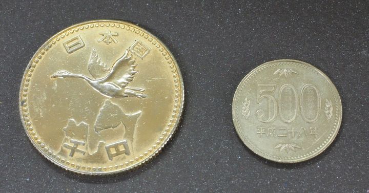 謎のメダル（左）と500円硬貨の比較。「日本国」「千円」の刻印が確認できる。